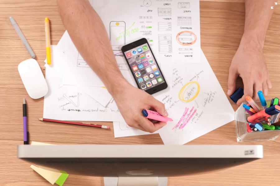 man sketching with highlighters next to a phone and a computer