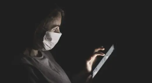 woman using smartphone in the dark wearing face mask