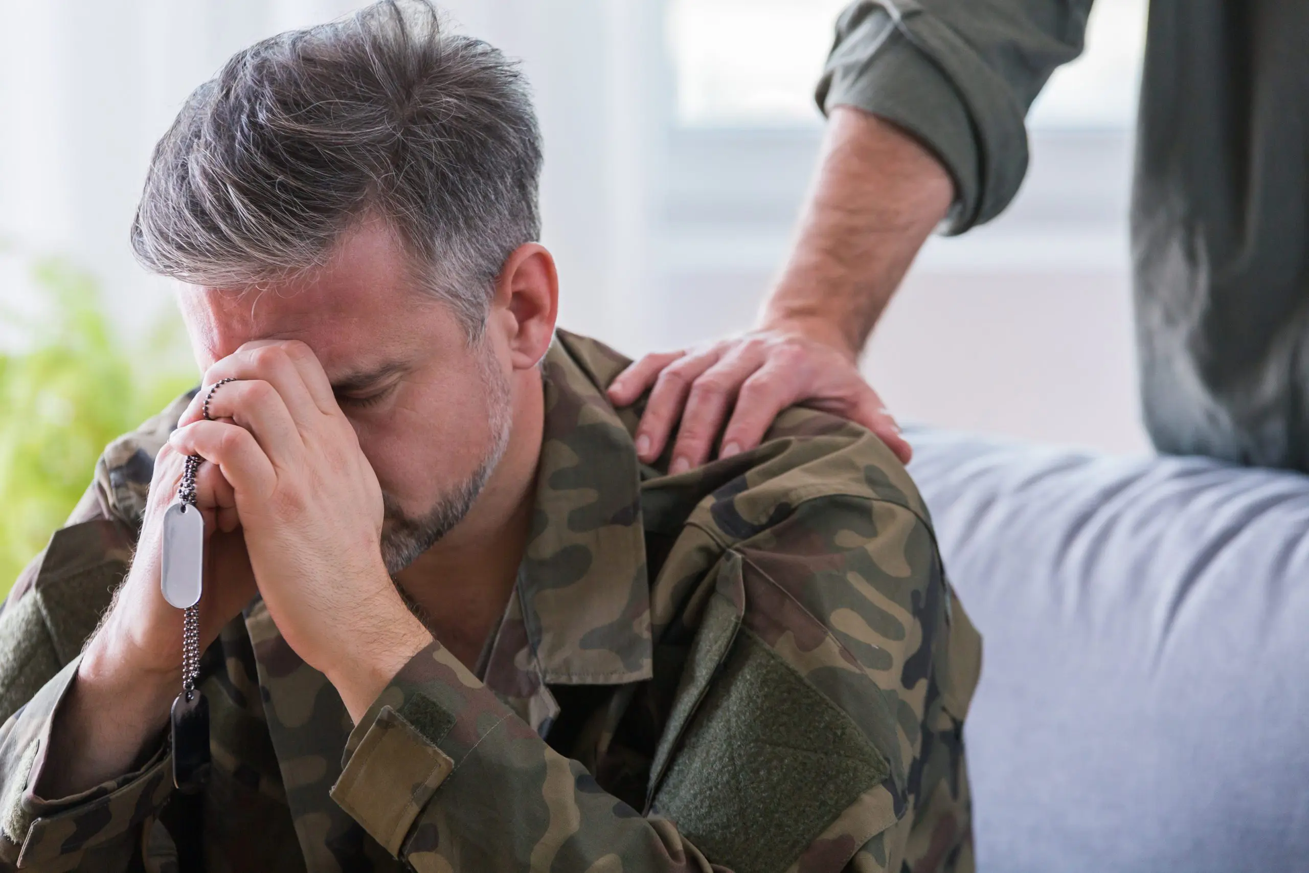 man in camouflage coat sits with his head in his hands
