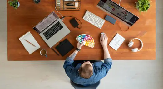 A person with a laptop and a screen working on a branding project, with colour swatches and a logo
