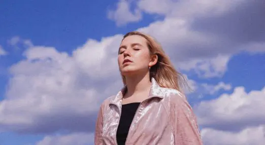 a young woman with her eyes closed, with a prominent background of the sky