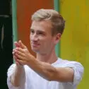 A picture of a white man with blond hair and a white t-shirt, extending his arms into a clap