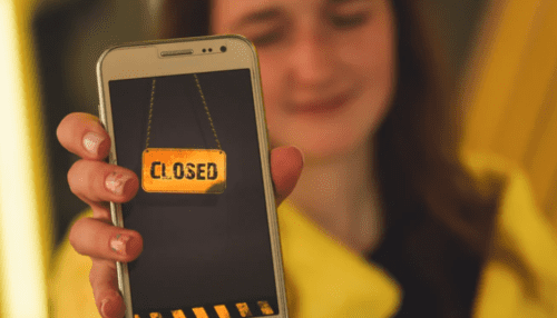 girl holding a phone with a 'closed' sign on it