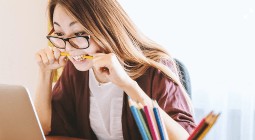 young woman biting pencils nervously staring at computer