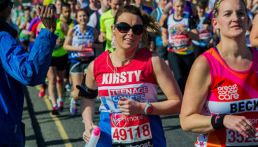 woman running a marathon in a teenage cancer trust vest