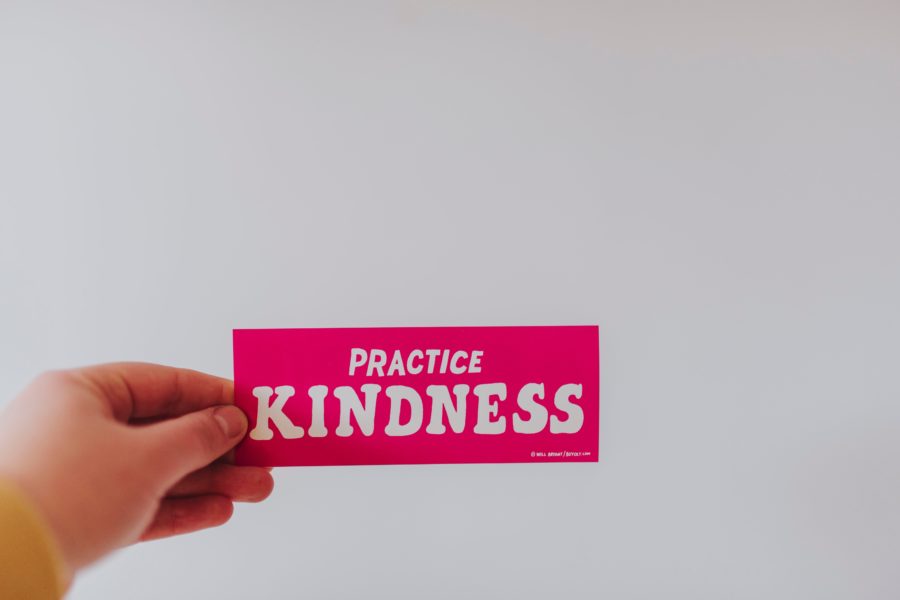 someone holding a card saying 'practice kindness'