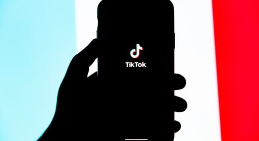 TikTok app running on an iphone held by a hand. The background is red, white and blue.