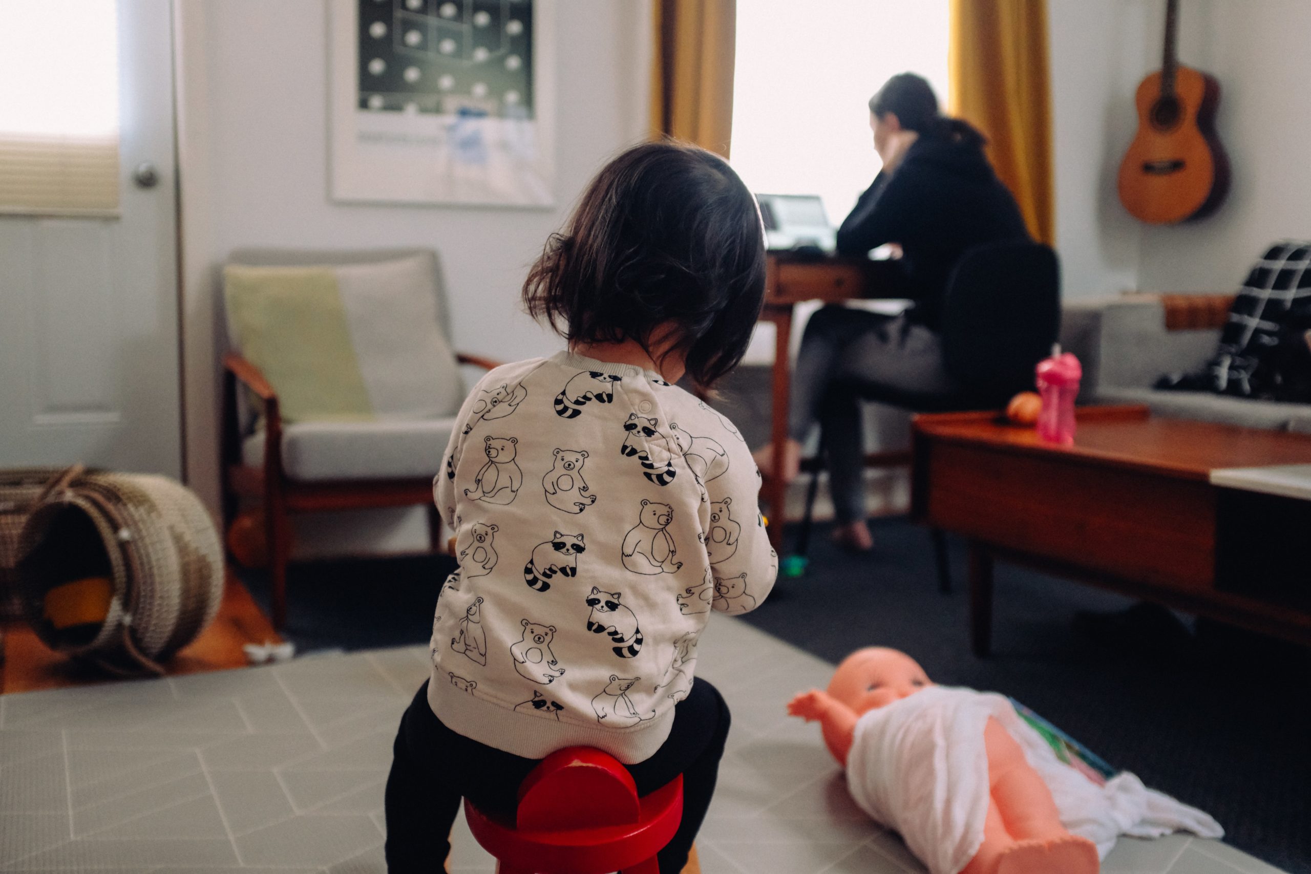 child playing in a living room while their parent works on a laptop