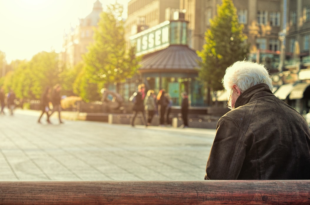 white haired man sitting on a bench in a town