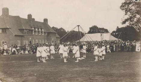 sepia photograph of children playing round a maypole in a garden