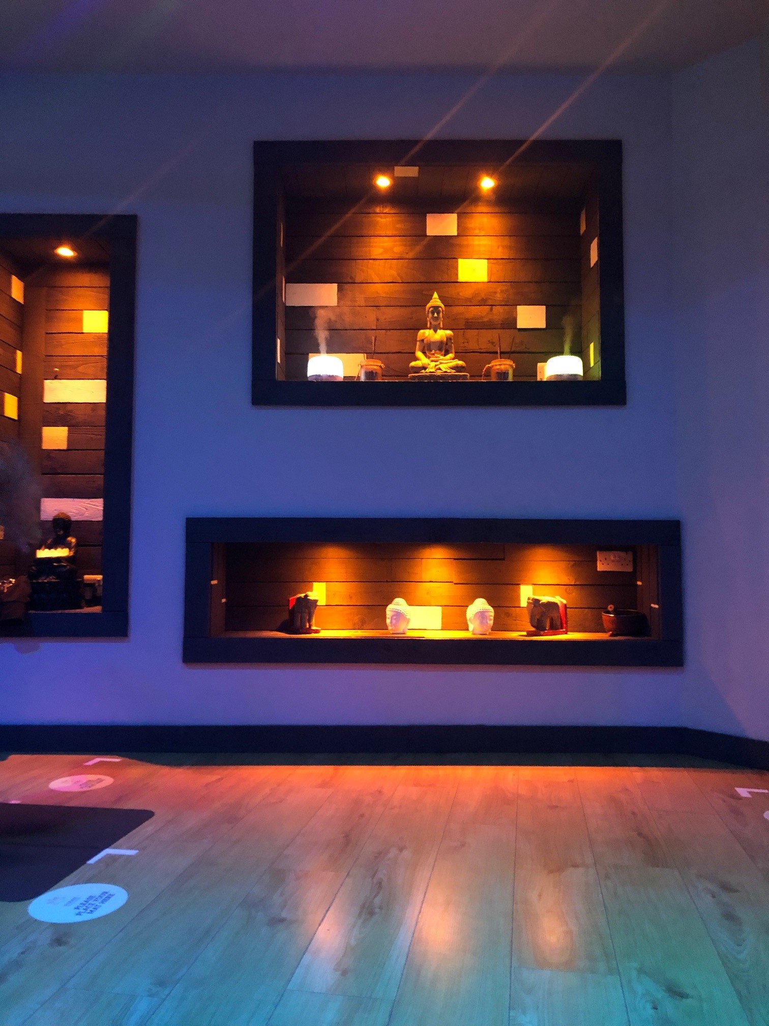 a yoga room with a purple wall containing lit up shelves of buddhist statues