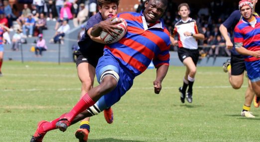 Young rugby player holding ball running whilst another player attempts to tackle him