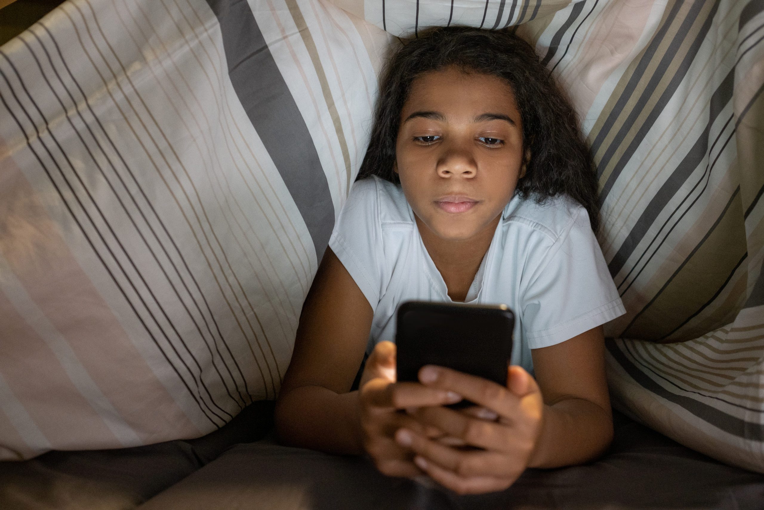 young girl on her phone under the duvet