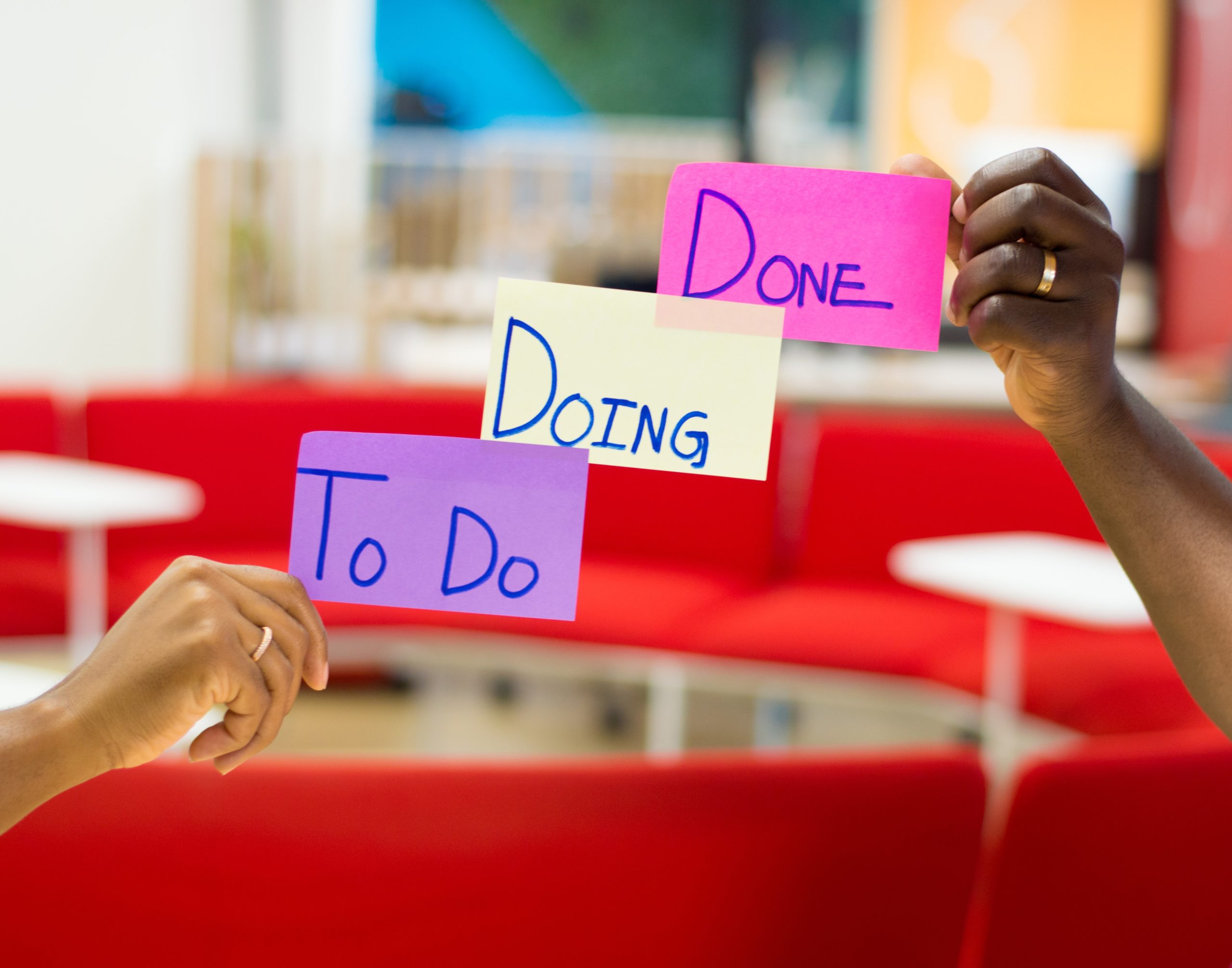 two hands holding coloured post-it notes saying the words To Do, Doing, Done