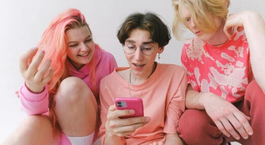 3 gen z people wearing pink looking at a phone